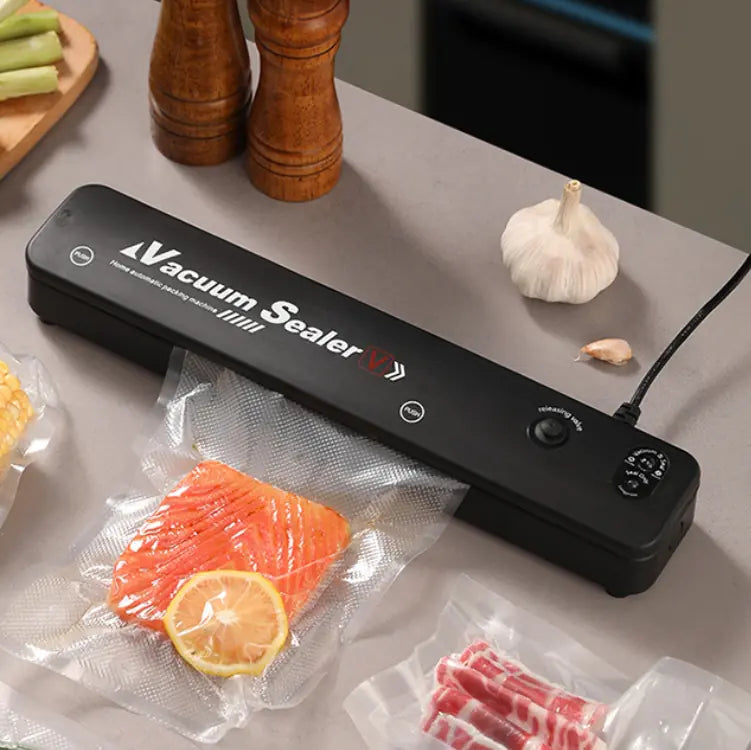 Compact black automatic vacuum sealer machine sealing a bag of fresh vegetables for long-term food preservation.